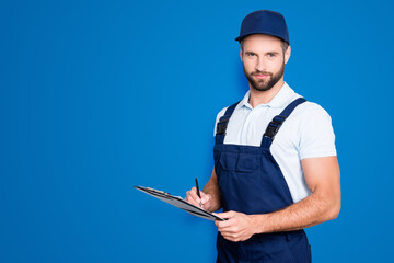 Canvas Print - Portrait with copyspace, empty place of virile harsh deliver in blue uniform having clipboard, pen in hands looking at camera isolated on grey background