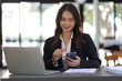 © Wasan - Young beautiful asian businesswoman in office working with laptop is using smartphone to work with electronic documents.