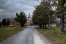 St. Joesph Catholic Church Apple Creek Missouri. A Rural Perry County Catholic Church At The End Of A Gravel Road. The Steeple Rises Between Two Evergreens. Winter Clouds Gather Above The Temple. 