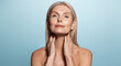 Elegant elderly woman, aging model, washing her face, rubbing nourishing skin lifting mask, using skincare cosmetic product, posing against blue background