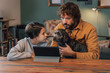 © Amparo Garcia - Bearded Caucasian man holds small black dog next to Hispanic girl while looking at tablet