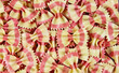 Full frame closeup of many bow tie butterfly shape pink yellow striped uncooked raw farfalle pasta noodles for seamless background