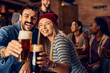 © Drazen - Young couple has fun while toasting with beer in bar and looking at camera.