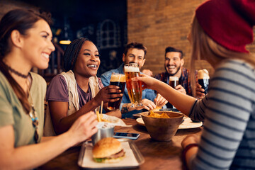 Wall Mural - Happy multiracial friends have fun while toasting with beer in pub.