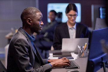 Side view portrait of serious black businessman using laptop at workplace in high tech IT security office