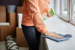 Close-up of young woman wiping dust from windowsill with rag during housework at home