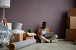 © Seventyfour - African American man sitting on the floor in the room and working online on laptop