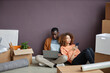 © Seventyfour - Young multiethnic couple using gadgets while resting on the floor among boxes during relocation
