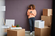 © Seventyfour - Young woman with curly hair communicating online on smartphone standing among boxes in the room