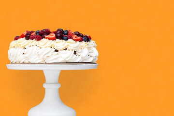 Wall Mural - Meringue Pavlova cake with whipped cream and fresh berries isolated, strawberries and blueberries on orange background. Horizontal orientation