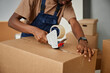 © Seventyfour - Close-up of African American worker in uniform packing boxes with adhesive tape