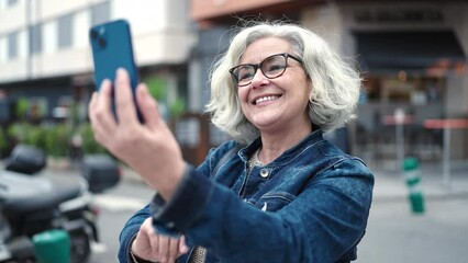 Wall Mural - Middle age woman with grey hair smiling confident having video call at street