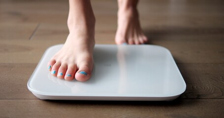 Young girl teenager steps on white scales to measure control weight. Teen checks body mass and fat, healthy dieting and fitness concept.