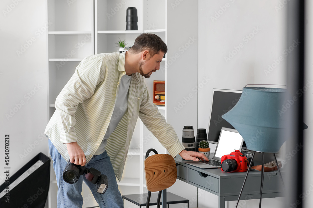 Male photographer with professional camera using laptop in studio