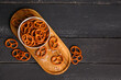 Board with bowl of tasty salted pretzels on dark wooden background