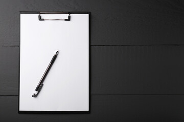 Clipboard with sheet of paper and pen on black wooden table, top view. Space for text