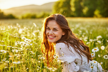 portrait of a beautiful woman in a white dress smiling at the camera sitting in a chamomile field ag