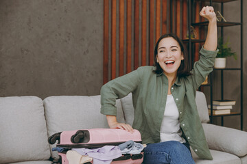 Wall Mural - Traveler woman wear casual clothes put thing into suitcase bag do winner gesture sit on grey sofa at home hotel. Tourist travel abroad in free spare time rest getaway. Air flight trip journey concept.