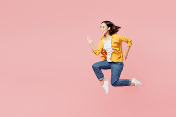 Wall Mural - Full body side view smiling excited fun cool young woman of Asian ethnicity wear yellow shirt white t-shirt jump high run fast hurry up isolated on plain pastel light pink background studio portrait.