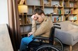 © nazariykarkhut - A young handsome man in a wheelchair looks out the window with a sad look