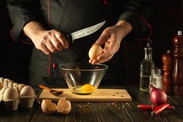 Cooking a delicious omelet for dinner with eggs in the kitchen of the restaurant. Egg and knife in the hands of the cook before breaking