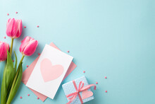 Mother's Day Concept. Top View Photo Of Bunch Of Pink Tulips Small Blue Giftbox With Ribbon Bow Envelope Postcard With Heart And Sprinkles On Isolated Pastel Blue Background With Copyspace