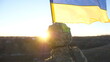 Dolly shot of male ukrainian army soldier lifting national banner in hill. Young man in military uniform waving flag of Ukraine against blue sky. Victory at war. Resistance to russian invasion concept