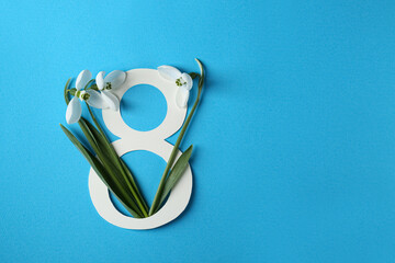 Wall Mural - Beautiful snowdrops and paper number 8 on light blue background, flat lay. Space for text