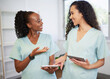 © Meeko Media - Two young women in the medical field wearing scrubs discuss with digital tablets