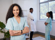 © Meeko Media - Portrait of nurse with curly hair arms folded, smiling - with team in background