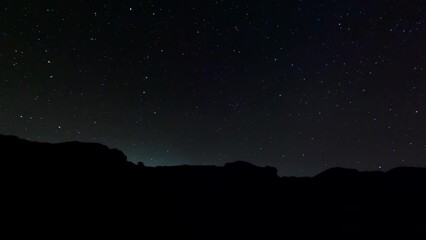 Starry nighttime time lapse with rugged landscape in silhouette in the foreground