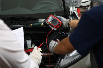 Wall Mural - Car repairman checking and testing car battery with digital electronic tester