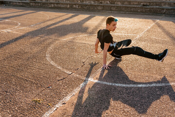 Teenage boy with blue hair breakdancing on a basketball court in the street. street dancer. youth culture and hip hop culture.