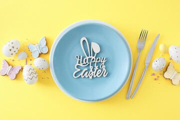 Wall Mural - Easter concept. Flat lay photo of blue plate with inscription happy easter colorful eggs cutlery fork knife butterfly shaped cookies and sprinkles on isolated yellow background