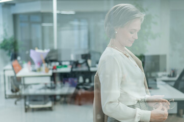 Portrait of a beautiful gray-haired caucasian woman in the office standing behind a glass wall. 