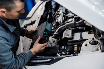 Wall Mural - An auto mechanic is fixing car under the hood at mechanic's workshop.