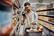 © Drazen - Young man using cell phone while shopping in supermarket.