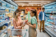 Supermarket worker assists her customer in choosing dairy product at refrigerated section.