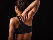 Female sporty muscular with ponytail doing stretching workout of the shoulders, blades in sport bra, holing the neck the hand on dark grey background with empty space.