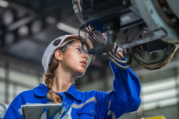 Wall Mural - woman engineer in uniform helmet inspection check control heavy machine robot arm construction installation in industrial factory. technician worker check for repair maintenance electronic operation