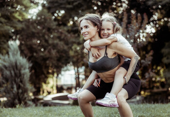 Athletic mom squatting with her little daughter outdoors, healthy lifestyle, fitness active family concept. Training together