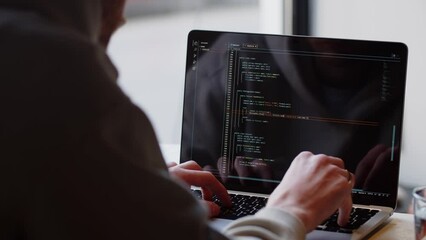 Rear view of a man writing code on his laptop. Close-up of a male web programmer working remotely while sitting in a cafe.
