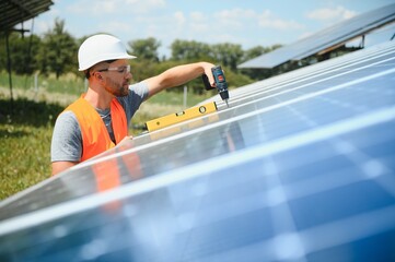 Wall Mural - Male engineer in protective helmet installing solar photovoltaic panel system. Alternative energy ecological concept.