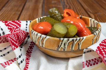 Wall Mural - Mixed pickles of cucumbers and red bell peppers. Pickles in Romanian traditional clay bowl on wooden table.