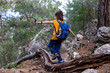 A boy in a bright yellow T-shirt walks through the forest with a backpack, balancing on a falling tree.