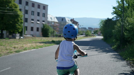 Wall Mural - One active small boy riding bicycle outside at green road in city bike lane. Back of child cyclist wearing helmet