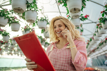 Wall Mural - Young woman working in a greenhouse and using a smartphone