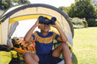 © Wavebreak Media - Happy african american boy sitting in tent and looking through binoculars in garden