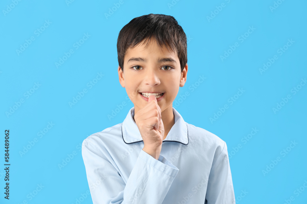 Little boy in pajamas biting nails on blue background