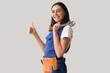 © Pixel-Shot - Female plumber with wrench showing thumb-up on grey background
